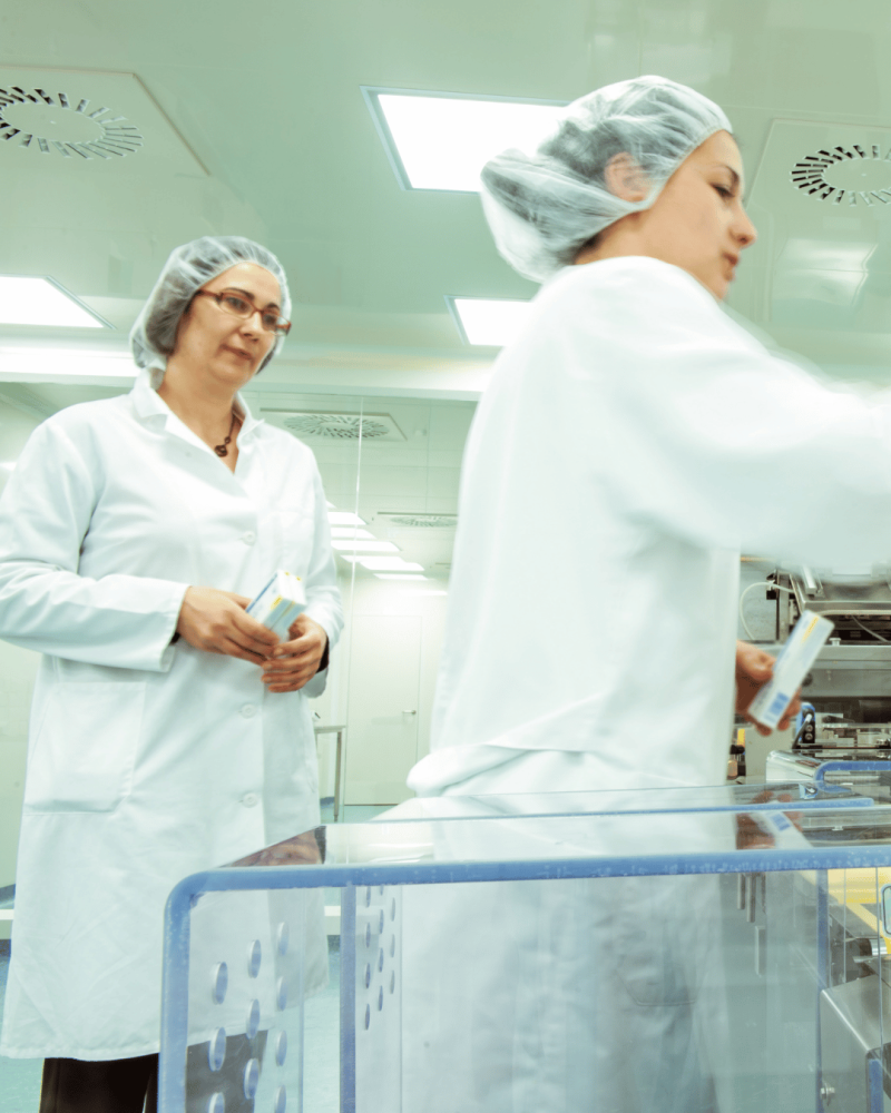 Two pharmaceutical machine operators wearing PPE in a laboratory setting.