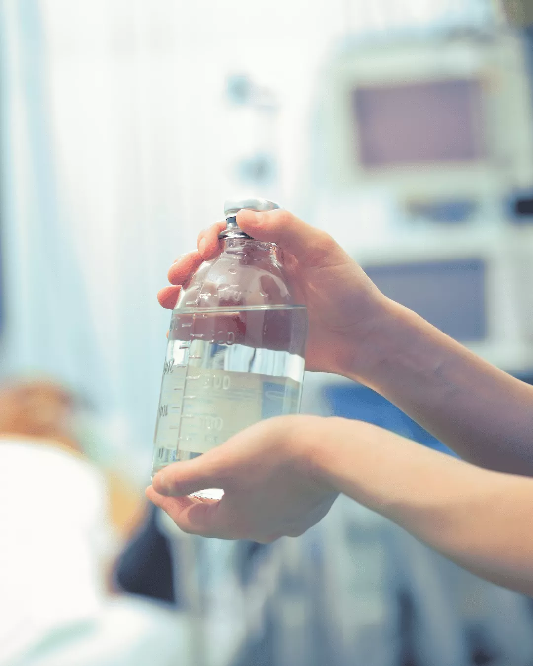 A transparent bottle full of liquid parenteral preparation being held by a nurse in a hospital setting.