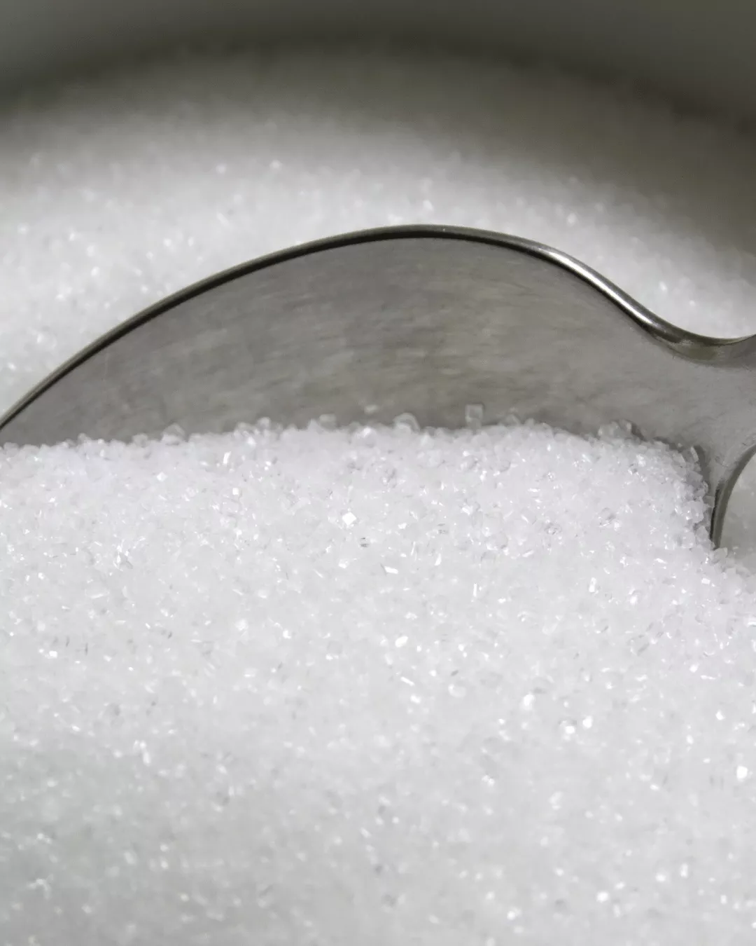 A close-up shot of granluated sugar with a spoon dipped in.