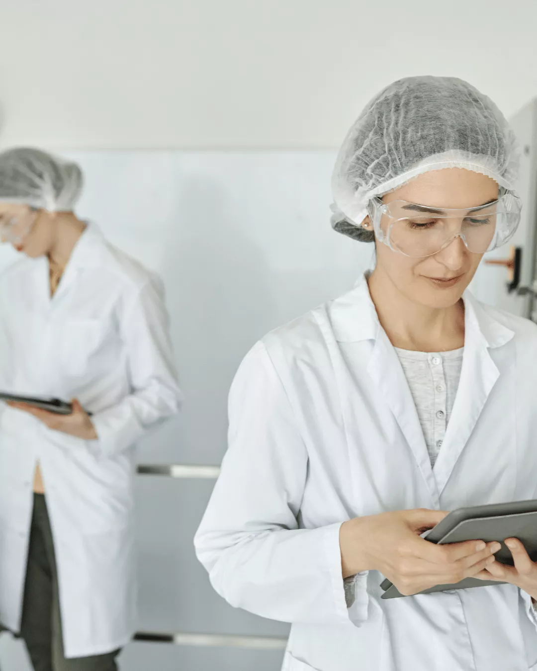 Two pharmaceutical manufacturing workers in a sterile lab environment wearing PPE.
